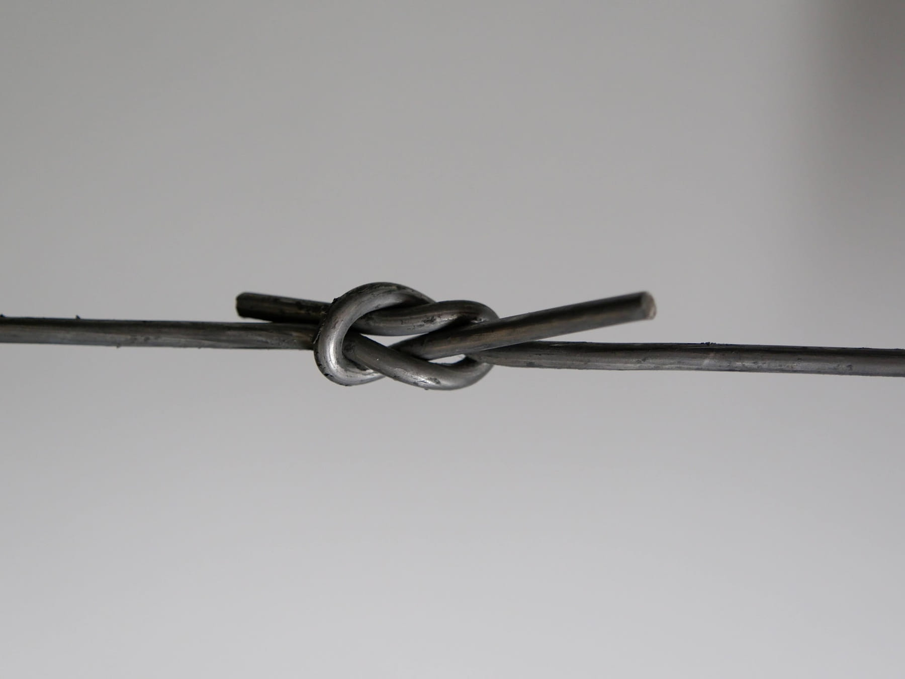 Baling wire tied in a flat reef knot against a grey background